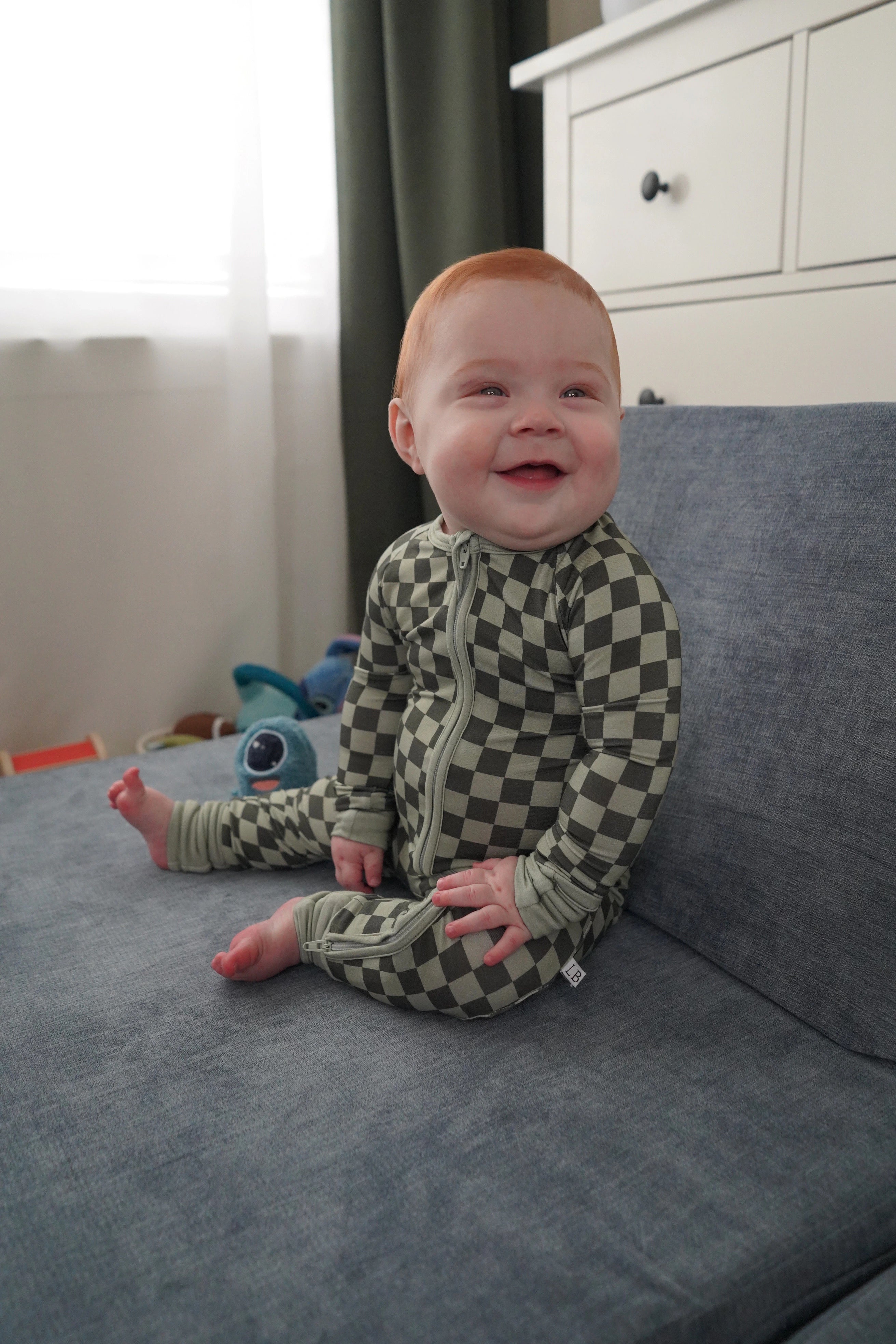 Baby in evergreen zippy sitting up on play couch.